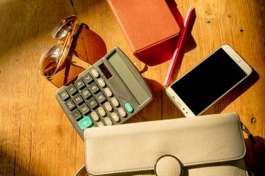 güneş gözlüğü, hesap makinesi, akıllı telefon, taşıma çantası ve çalışma kitabı masada