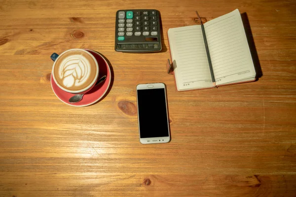 Heißer Mokkakaffee, Smartphone und Taschenrechner mit Arbeitsbuch auf dem Holztisch — Stockfoto