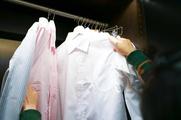 Ženy vybrat Pánské košile na ramínko, visí ve skříni — Stock fotografie