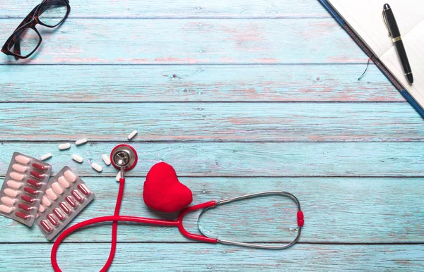 Hälsovård och medicinska begrepp röd stetoskop och medicin på den blå trä bakgrunden — Stockfoto