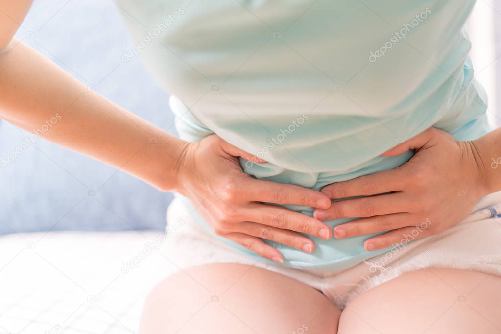 Young woman suffering from abdominal pain while sitting on the sofa and feeling stomach ache, symptom of pms