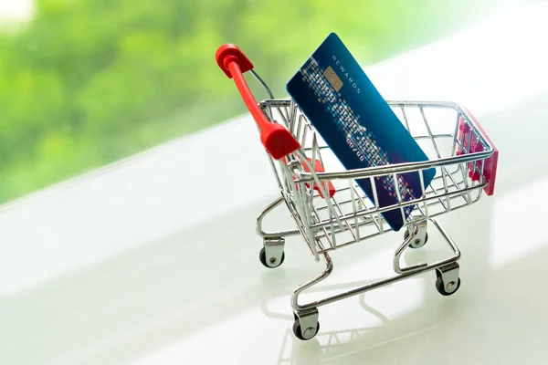 Credit card op het winkelwagentje van de kar op witte tafel met een groene achtergrond — Stockfoto