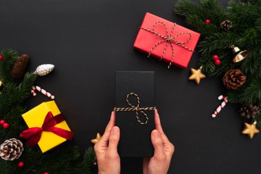Noel hediyesi kutusunda çam ağacı ve siyah arka planda Noel süsü var.