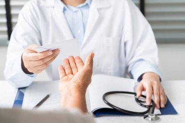Doktor tanıyı yazıyor ve yaşlı kadın hastaya reçete yazıyor.