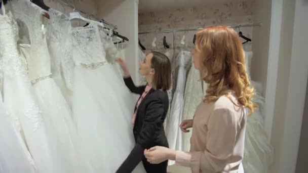 Žena se snaží na svatební šaty v obchodě s ženy asistent. — Stock video