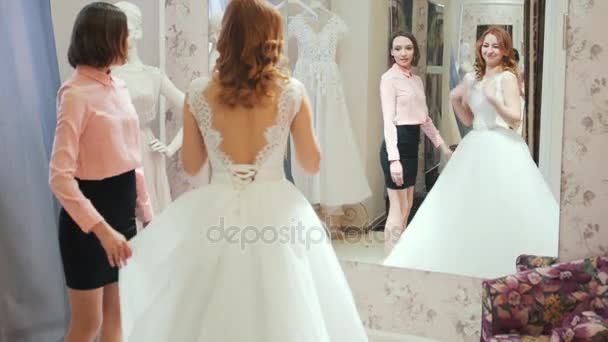 Femme essayant sur robe de mariée dans un magasin avec des femmes assistant . — Video