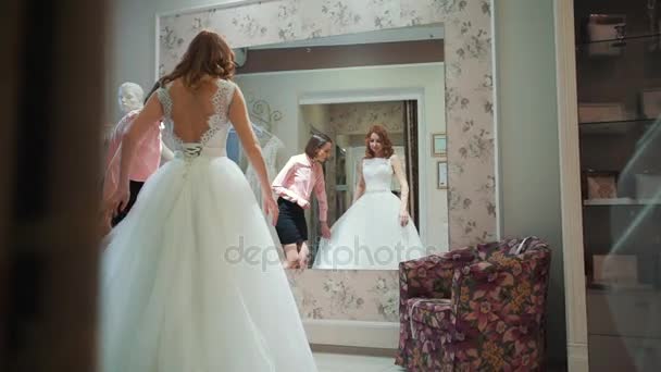 Жінка намагається на весільній сукні в магазині з помічницею жінки . — стокове відео
