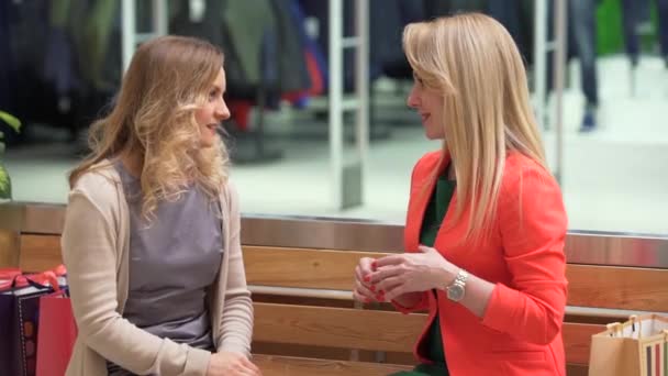 Two excited shopping woman resting on bench at shopping mall — Stock Video