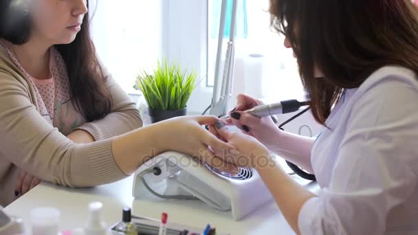 Primer plano de manicura de hardware en un salón de belleza. Manicura está aplicando taladro de lima de uñas eléctrica a la manicura en el dedo femenino — Vídeo de stock