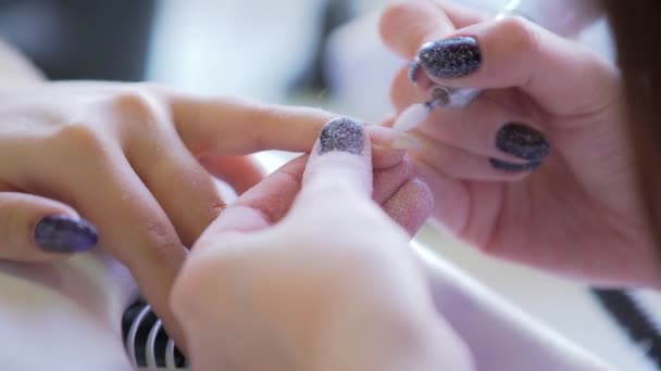 Master makes hardware manicure. Manicurist is applying electric nail file drill to manicure on female fingers — Stock Video