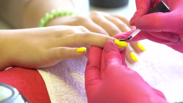 Primer plano de un esteticista aplicando esmalte de uñas a las uñas femeninas en un salón de uñas. Primer plano de una mano de mujer con esmalte de uñas amarillo después de la manicura . — Vídeo de stock