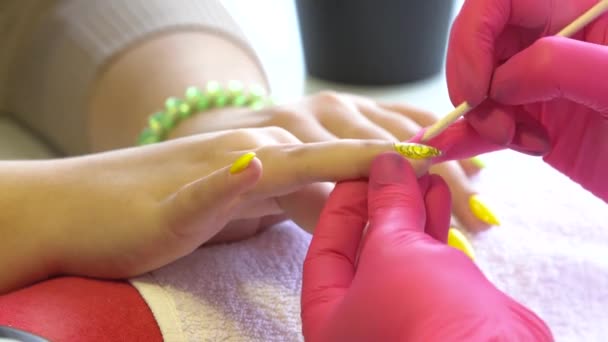 Primo piano di un estetista che applica lo smalto per unghie femminili in un salone di bellezza. Primo piano di una mano di donna con smalto giallo dopo la manicure . — Video Stock