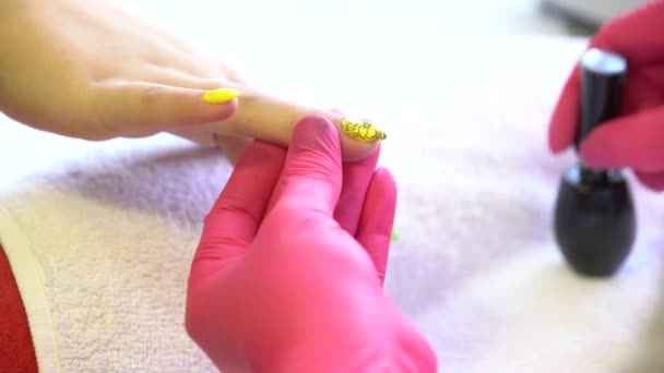 Close-up shot van een schoonheidsspecialiste nagellak op vrouwelijke nagel in een nagel salon toe te passen. Close-up van de hand van een vrouw met gele nagellak na de manicure. — Stockvideo