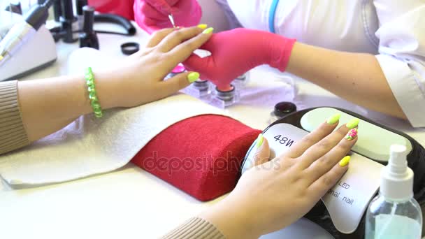 Primer plano de un esteticista aplicando esmalte de uñas a las uñas femeninas en un salón de uñas. Primer plano de una mano de mujer con esmalte de uñas amarillo después de la manicura . — Vídeo de stock