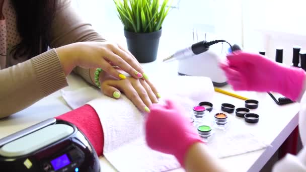 Close-up shot van een schoonheidsspecialiste nagellak op vrouwelijke nagel in een nagel salon toe te passen. Close-up van de hand van een vrouw met gele nagellak na de manicure. — Stockvideo