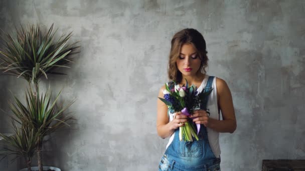 Tjej med blont hår och en massa blommor tulpaner, rosor, på en grå bakgrund — Stockvideo