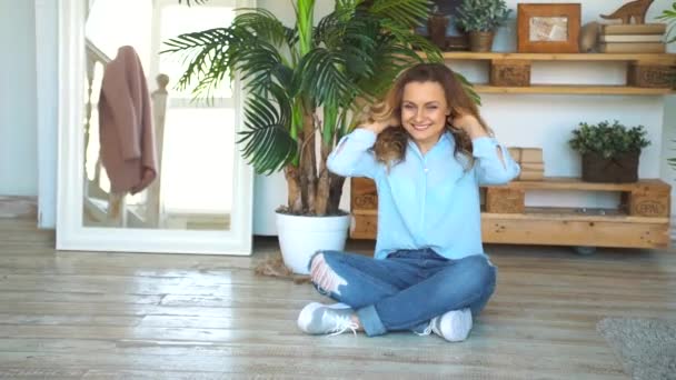 Счастливая взрослая женщина, сидящая на полу своего дома с руками на коленях — стоковое видео