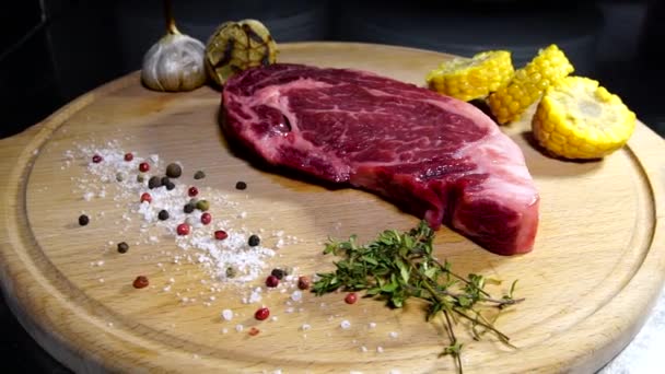 Carne crudă. O bucată mare de cotlet de carne de vită pe o placă de tăiere cu rozmarin și condimente . — Videoclip de stoc