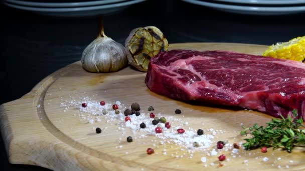 Carne cruda. Un trozo grande de chuleta de res en una tabla de cortar con romero y especias . — Vídeo de stock