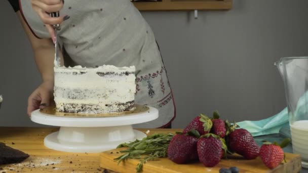 El confitero decora el pastel y lo cubre con crema de mantequilla. Herramientas de confitería: espátula para crema de alineación. Pastel de esponja de chocolate con crema de mantequilla . — Vídeo de stock