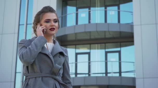Eine schöne junge kaukasische Geschäftsfrau, die vor einem Bürogebäude spaziert — Stockvideo