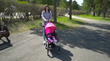 Genç anne ile bebek arabasını Park yürüme