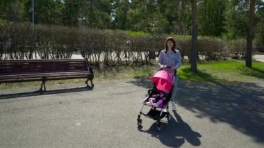 Genç anne ile bebek arabasını Park yürüme