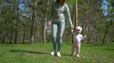 Genç bir anne kızının yürümeyi öğretiyor. Parkta yeşil çimenlerin üzerinde.