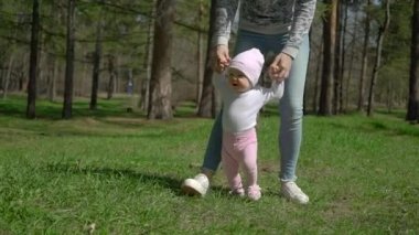 Genç bir anne kızının yürümeyi öğretiyor. Parkta yeşil çimenlerin üzerinde.