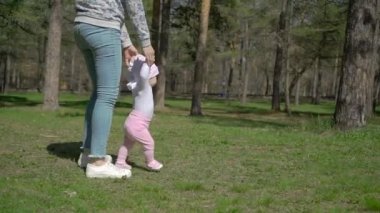 Genç bir anne kızının yürümeyi öğretiyor. Parkta yeşil çimenlerin üzerinde.