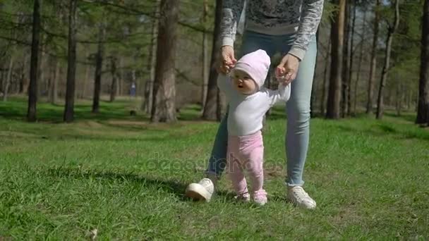 Egy fiatal anya lánya tanít, hogyan kell járni. A parkban, a zöld fű. — Stock videók