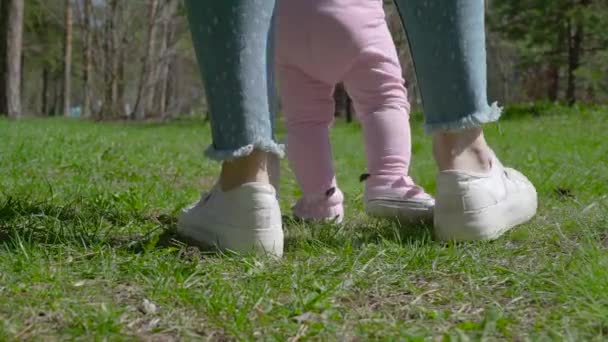 Een jonge moeder leert haar dochter hoe te lopen. In het park op het groene gras. — Stockvideo