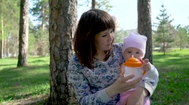 Açık havada yürüyüşe şirin bir bebek portresi. Çocuk oturur ve suyu şişeden içer.