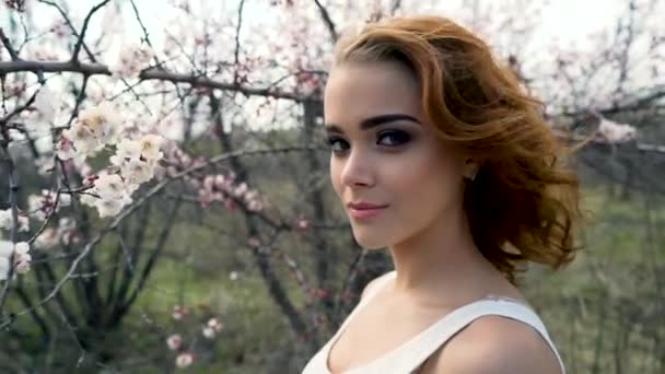 Vacker ung brunett flicka sitter i en blommande cherry orchard. — Stockvideo