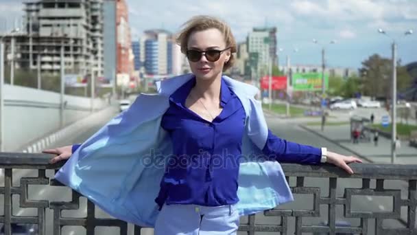 Belle femme d'affaires en costume d'affaires avec des lunettes et une coupe de cheveux courte, se tient sur le pont. Circulation des voitures . — Video