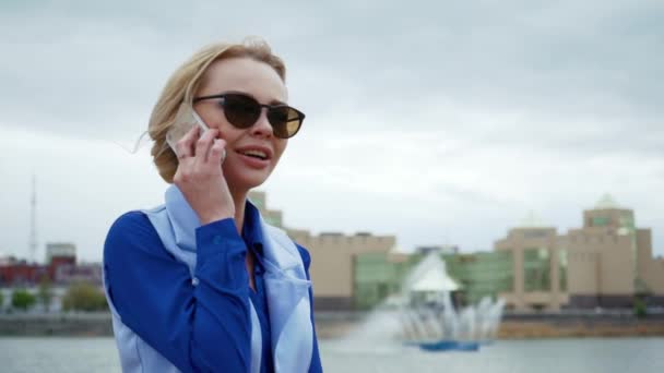 Jeune femme blonde séduisante marchant dans le parc au bord de la rivière et parlant sur le téléphone portable. Chemise bleue, costume d'affaires . — Video