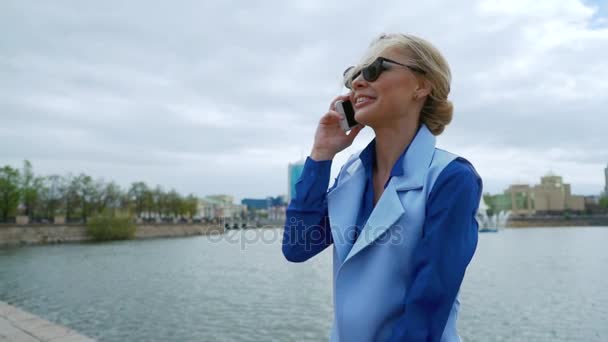 Крупним планом фото усміхненої бізнес-леді, яка використовує мобільний телефон у місті поруч з річкою . — стокове відео