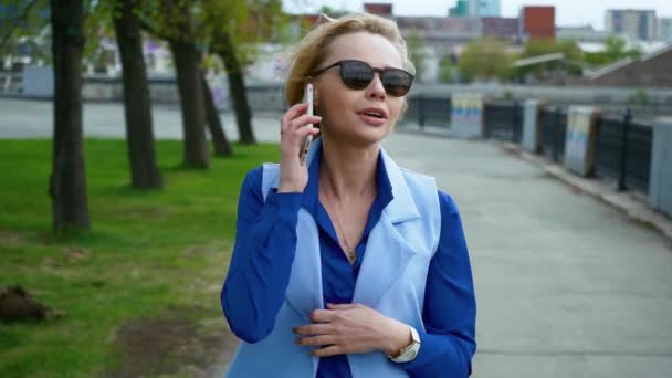 Photo rapprochée d'une femme d'affaires souriante utilisant un téléphone portable dans la ville près de la rivière . — Video