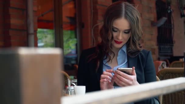 Junge gut gekleidete Frau mit perfekter Figur, die während des Frühstücks auf der Restaurantterrasse auf ihren Smartphone-Bildschirm schaut, Frau surft im Internet auf ihrem Touchscreen-Handy im Café — Stockvideo