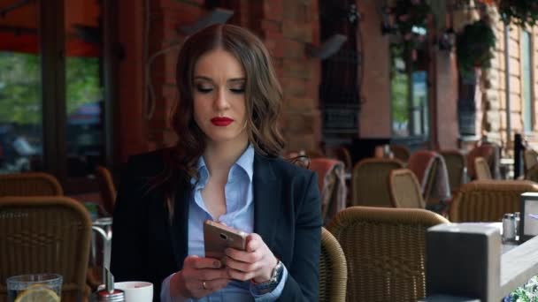 Привлекательная деловая женщина в костюме, используя смартфон в открытом кафе, пьет кофе. Медленное движение. Профессиональная деловая женщина разговаривает по мобильному телефону на открытом воздухе. Деловая жизнь города — стоковое видео