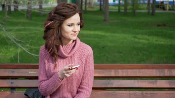 Prstenec záběr ženské dospívající dívka mluví o telefonu sedí na lavičce v jarní slunečný den, uhd prores záznam — Stock video
