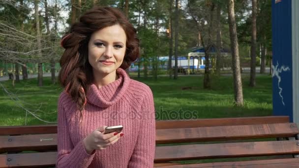 Gimbal shot of female teen girl talking on the phone sitting on bank in spring sunny day, uhd prores footage — Stockvideo