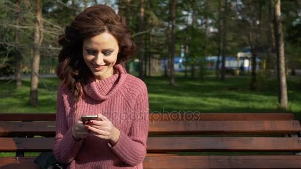 Teen kız bahar güneşli bir günde, uhd prores görüntüleri bankta oturan telefonda konuşurken fotoğrafını gimbal — Stok video