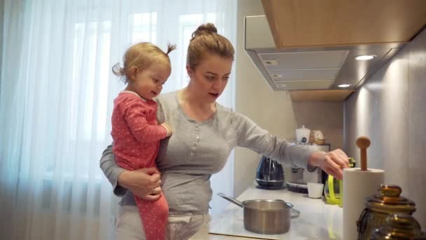 Няня с младенцем в руках готовить смесь блюдо в горшке и вкус его ложкой . — стоковое видео