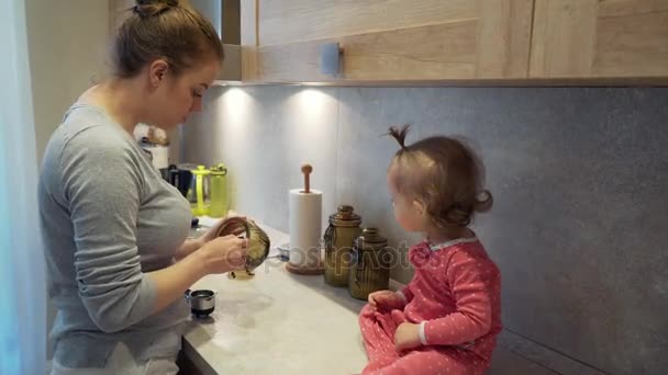 Kuchaři šťastné mladé matky s dítětem, který sedí na stole doma kuchyň — Stock video