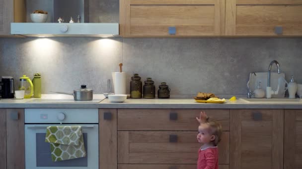 Bebê olha para fora de debaixo da mesa, astutamente olha em volta e rouba uma comida da mesa . — Vídeo de Stock