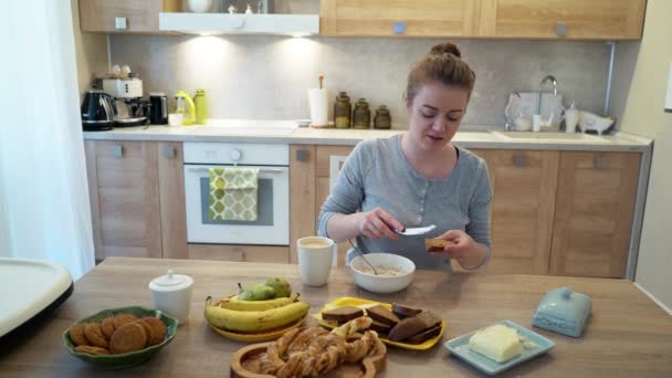 Flickan är att ha frukost i köket. Bröd och spannmål på bordet — Stockvideo