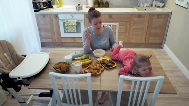 Familie, voedsel, kind, voeding en conceptie van vaderschap - gelukkige jonge moeder ontbijten met baby zittend op tafel thuis, eten kaas — Stockvideo