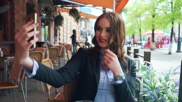 A luxurious young girl in a business suit makes herself selfie in a cafe. — Stock Video