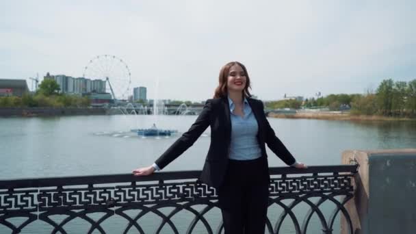 Retrato de uma jovem mulher de negócios feliz de pé com a mão dobrada contra o fundo da cidade urbana — Vídeo de Stock